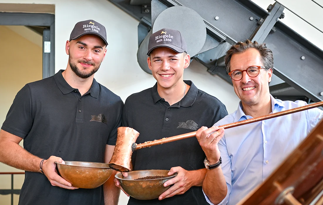 Die Eishockey Spieler Max Glötzl und Philipp Krauß stehen mit Sebastian Priller am Sudkessel
